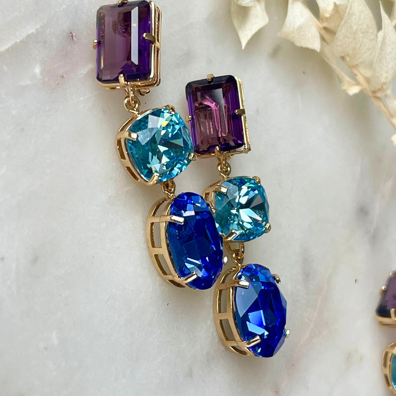 Ein Paar goldfarbene Clip-Ohrringe, ausgestattet mit austauschbaren Hängekristallen in Violett, Aquamarin- und Saphirblau, die für vielseitigen Glanz und Eleganz sorgen.