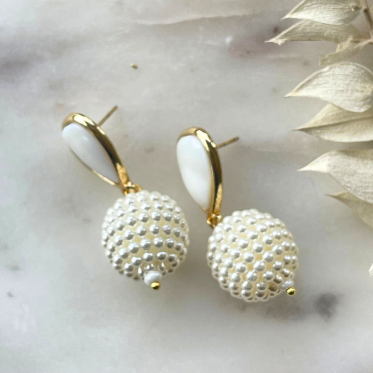 Die 'Perlen Ohrringe Little DAISY' sind exquisite Ohrringe mit einem Stecker-Verschluss. Die Permutt-Basis hat eine Breite von 1,5 cm, während die Gesamtlänge, einschließlich Basis und Anhänger, etwa 4 cm beträgt. Diese eleganten Ohrringe bestehen aus 18 K vergoldetem Messing in Kombination mit Permutt.
