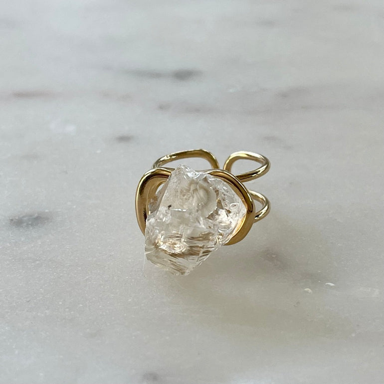 Der Ring "ÉRIKA", vergoldet mit 18 K Bergkristall, ist ein unverwechselbares Stück.  Ein offener Cocktailring in transparentem Design. Verstellbar.  Aus hochwertigem, 18 K vergoldetem Messing mit natürlichem Bergkristall. Perfekt für Frauen, die besondere und einzigartige Stücke zu schätzen wissen.