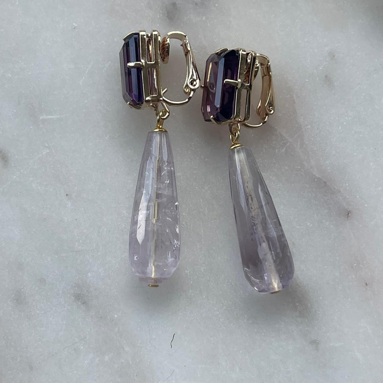 Ohrclip LE CLOS NORMAND: Eleganter und vielseitiger Schmuck mit grünen und lila Kristallen. Clip-Verschluss, Länge: 6,7 cm, Breite: 1,1 cm. 18 K vergoldetes Messing mit funkelnden Kristallen in den Farben Lila und Smaragd. Enthält ein komplettes Ohrring-Paar sowie zusätzliche lila Kristalle für vielseitiges Styling