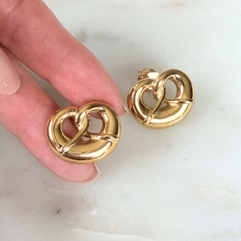 Goldfarbene Brezel-Ohrringe in der Hand gehalten – zeigt Größe, Form und den warmen Glanz der Oberfläche