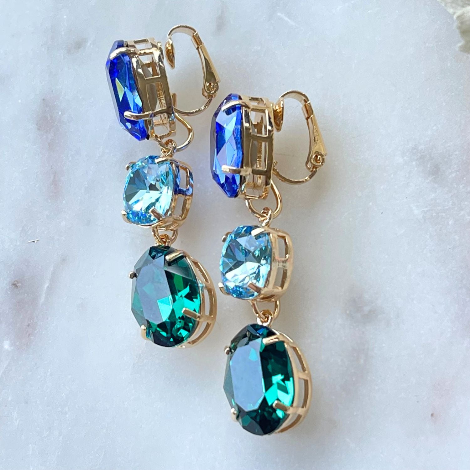 Erleben Sie die Eleganz der "GLOW"-Ohrringe mit blau-grünen Kristallen. Die grüne Basis kann separat getragen werden und verleiht einen dezenten, dennoch wunderschönen Touch. Die weltberühmten Kristalle sorgen für Glanz und zeitlose Eleganz